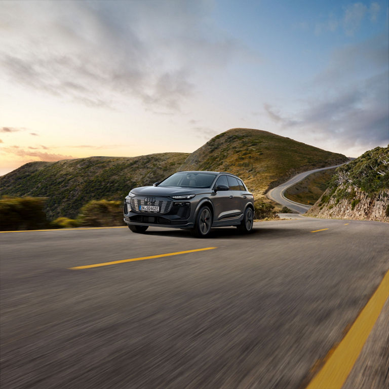 Three-quarter front view of an Audi SQ6 e-tron in motion along a mountain-side road