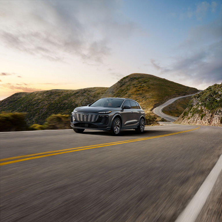 Three-quarter front view of the Audi SQ6 e-tron accelerating on an hill road.