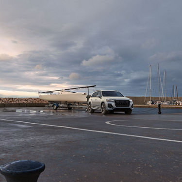 Three-quarter front view of the Audi Q7 parked with a boat attached to the trailer hitch.