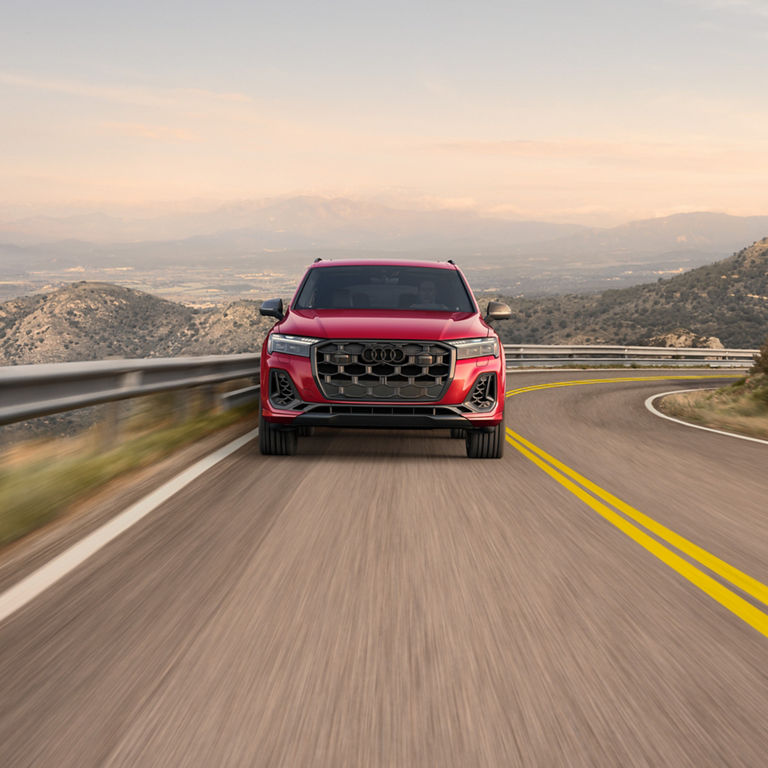 Front profile of a red Audi SQ7 accelerating on a mountain-side road.