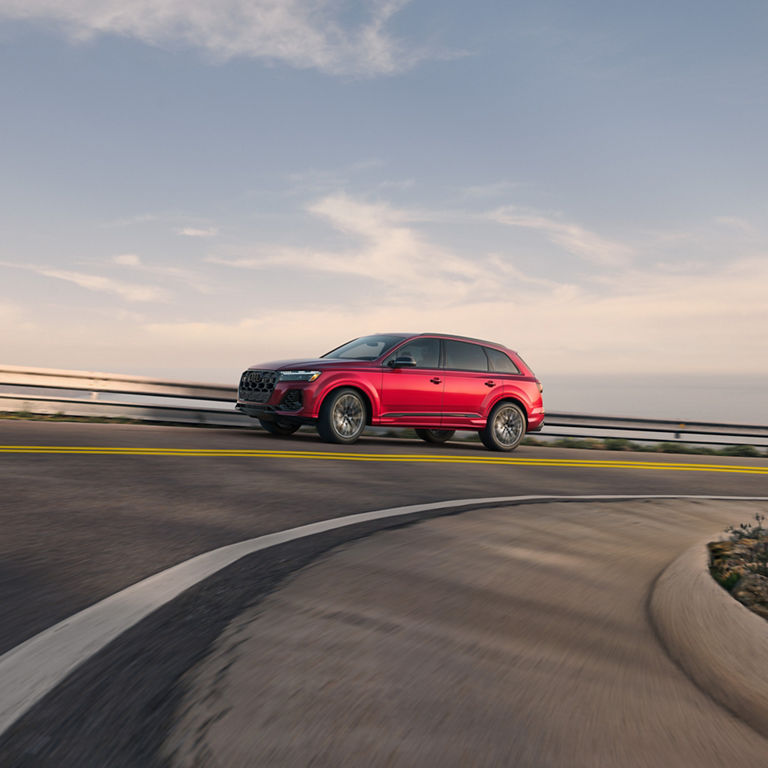 Side view of a red Audi SQ7 accelerating on a mountain-side road. 