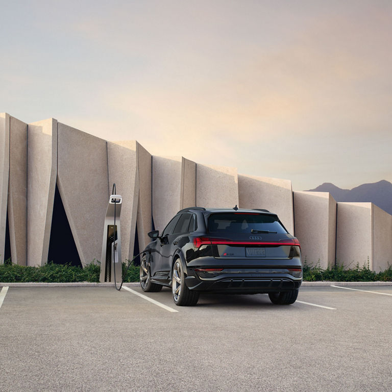 Rear-view of the Audi SQ8 e-tron parked and charging in front of a building.