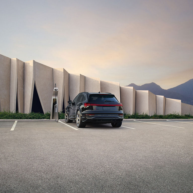 Rear-view of the Audi SQ8 e-tron parked and charging in front of a building.