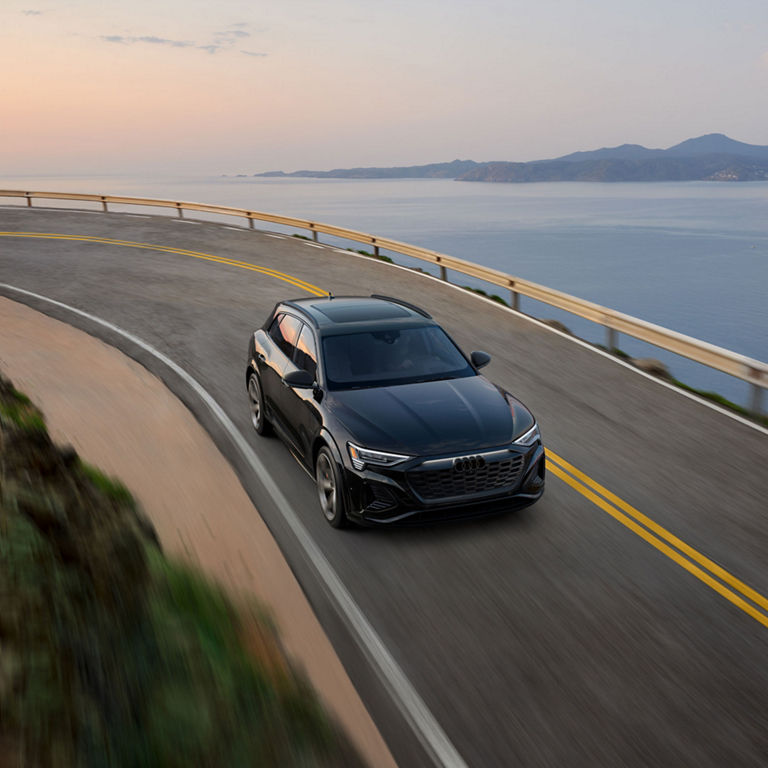 Aerial front-view of the Audi SQ8 e-tron accelerating on an oceanside road.