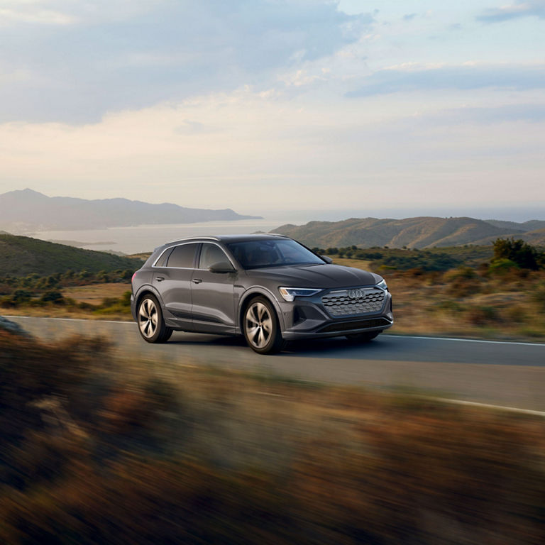 Three-quarter side profile of a gray Audi Q8 e-tron accelerating.