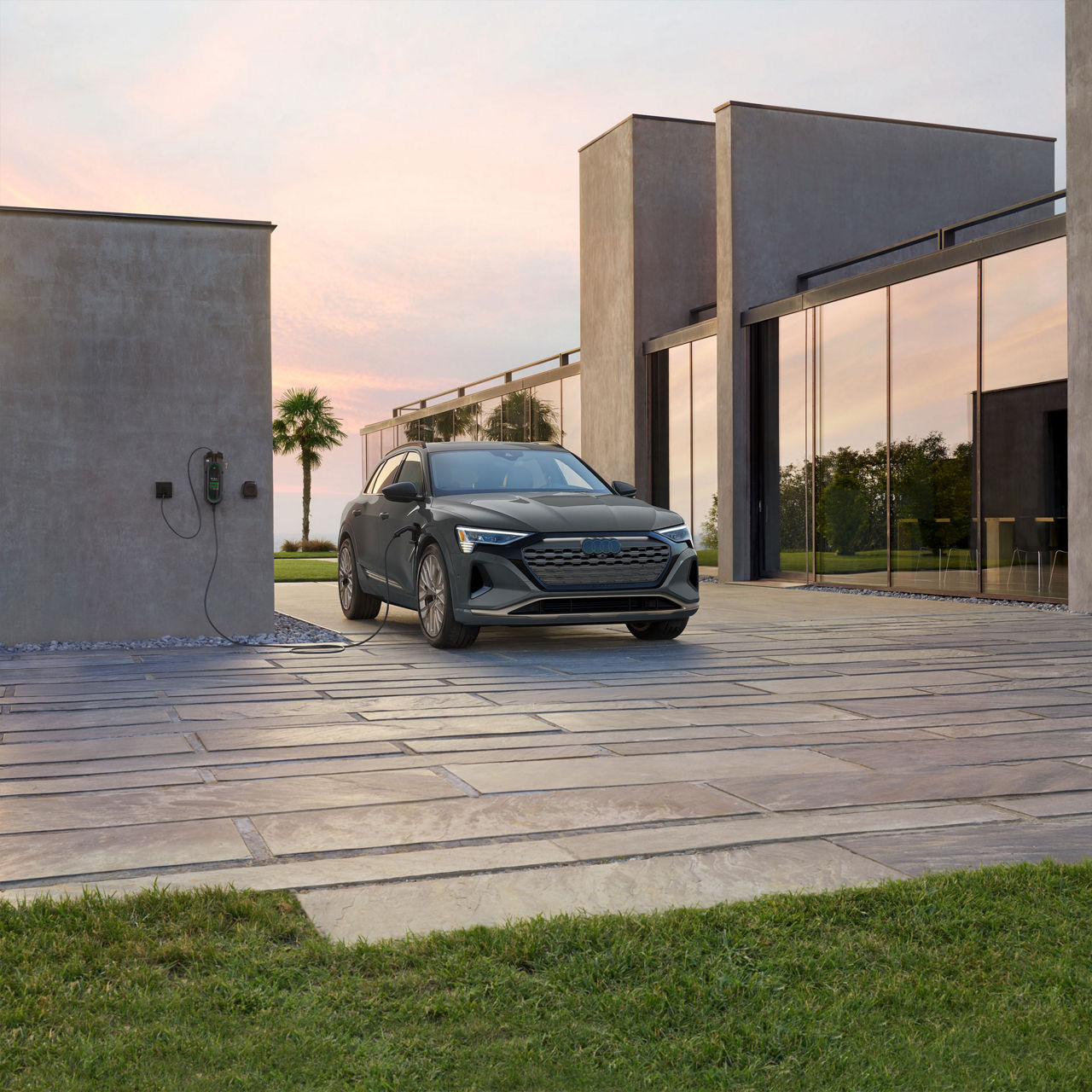 Three-quarter front profile of a gray Audi Q8 e-tron parked and charging on a driveway. 
