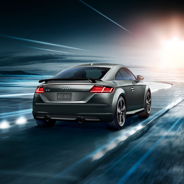 Three-quarter rear profile of the Audi TT Coupe accelerating.