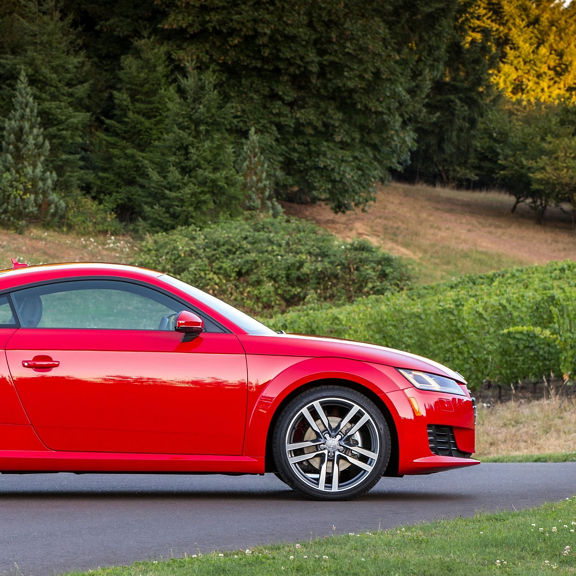 Side view of a red Audi TT Coupe parked in front of a grassy hill.