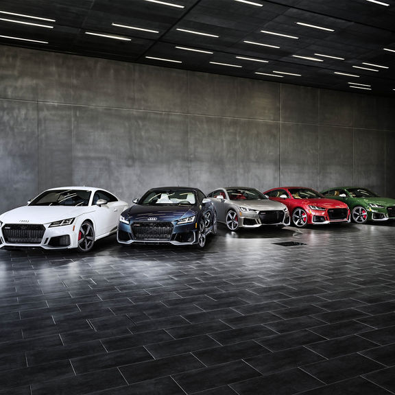 A lineup of Audi TT vehicles parked in a grey room.