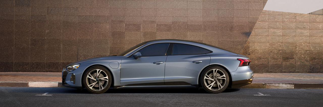 Side profile of an Audi e-tron GT parked in front of a tiled wall. 