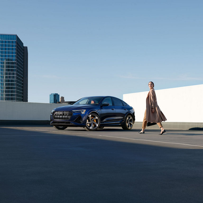 Three-quarter front profile of the Audi e-tron® S Sportback with a woman walking beside.