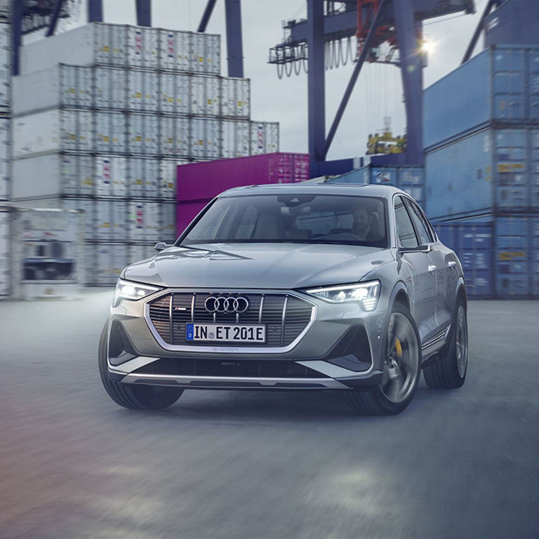 Front profile of the Audi e-tron® Sportback accelerating with headlights on.