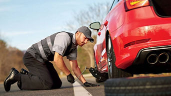 An Audi technician replacing a tire on the side of a road.