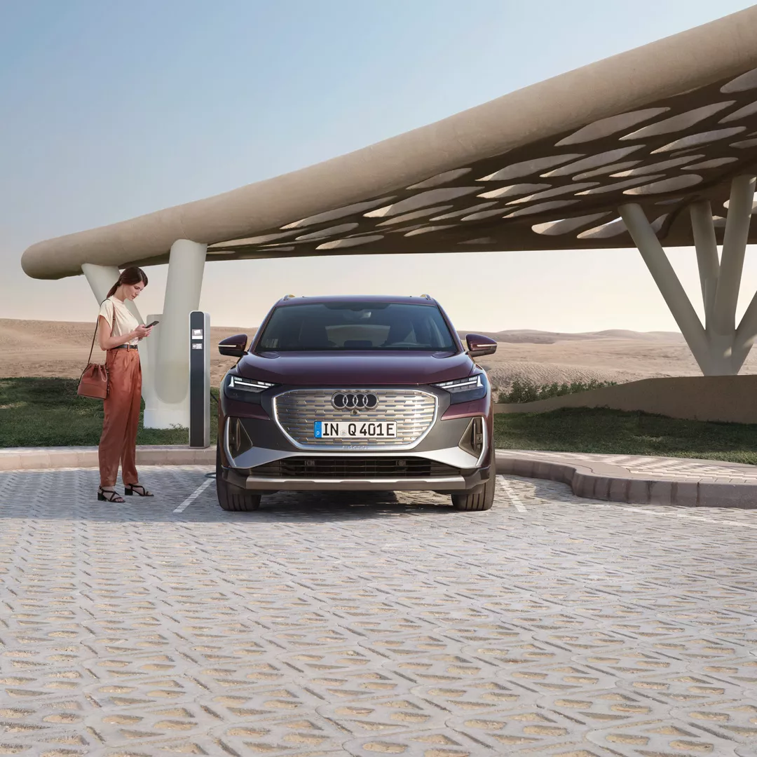 A woman checking the charging status of her Q8 e-tron vehicle as it's plugged in next to her. 