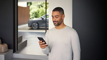 A man is looking at his phone screen. An Audi model is parked in the background.