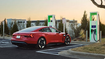 A red Audi RS e-tron GT plugged into a charging station at sunset. 