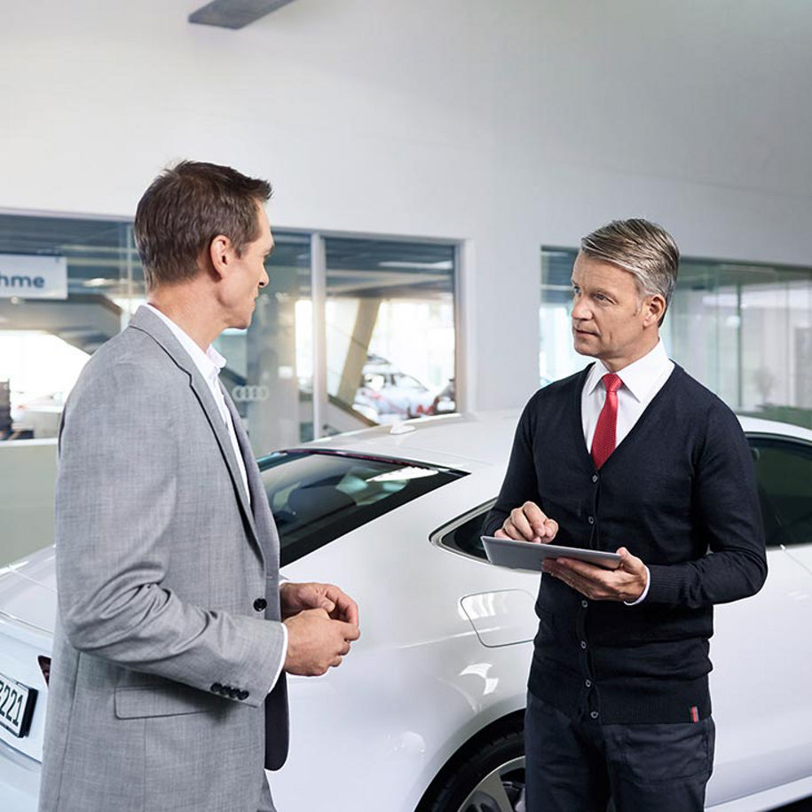 A mid-shot photo of two men talking in an Audi dealership.