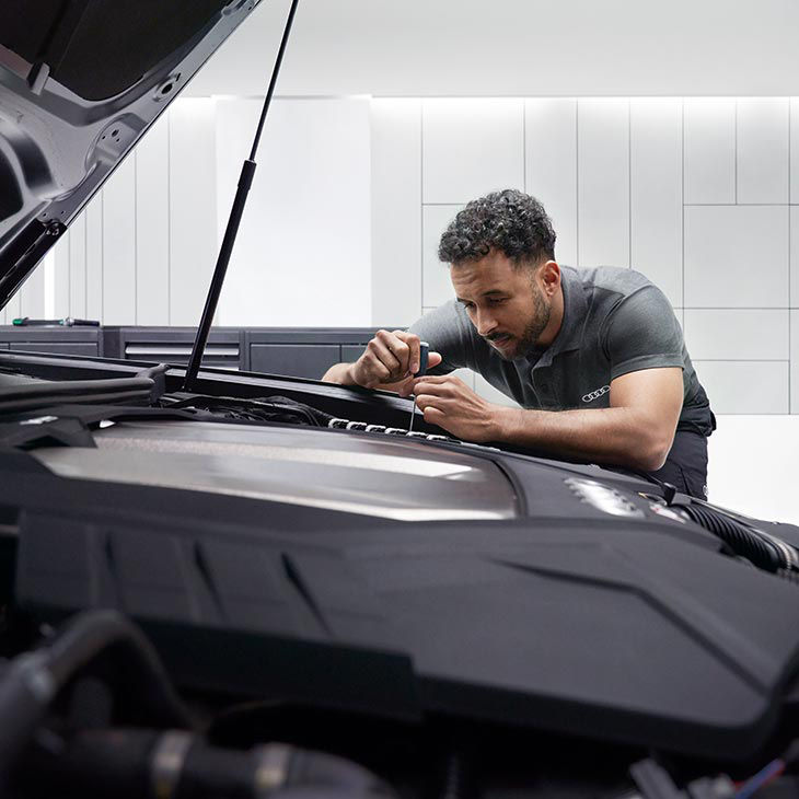 A photo of an Audi Certified Technician under the hood of an Audi vehicle to fix it.