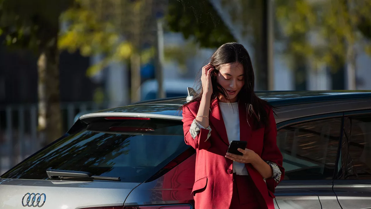 A woman on her phone next to her Audi vehicle. 