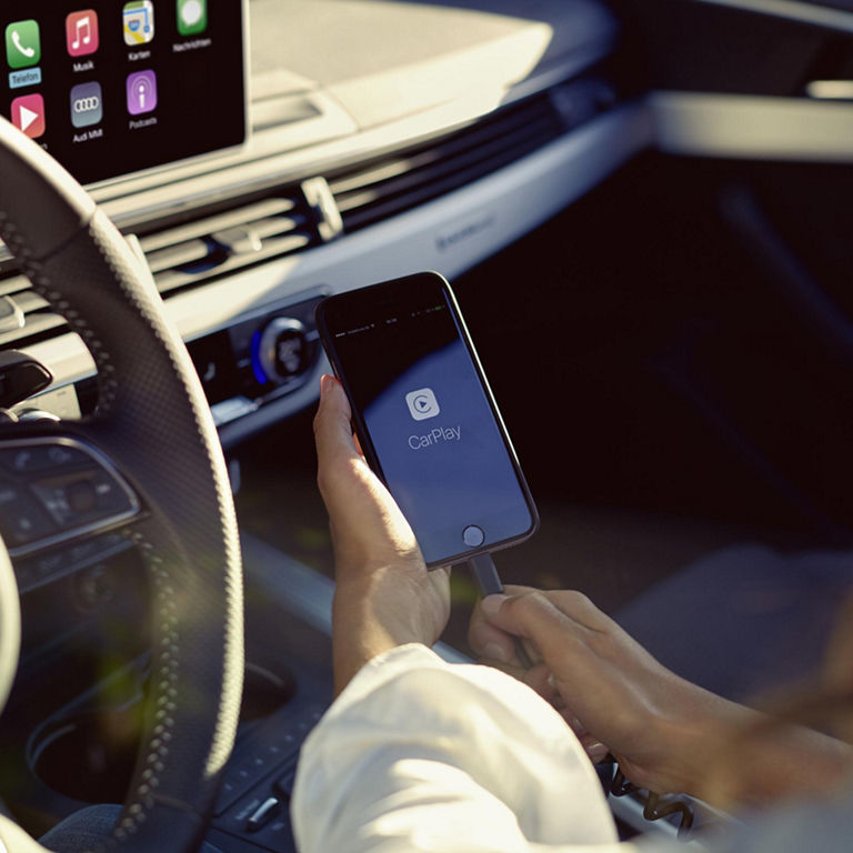 Person plugging a cable into iPhone displaying the Apple Car Play logo.