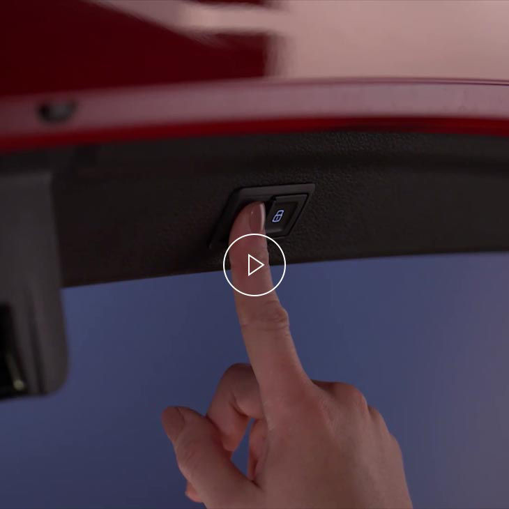 A close-up photo inside an Audi vehicle showing a finger about to press the rear hatch button.