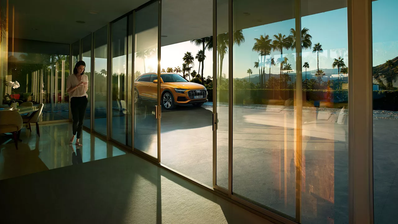 Woman looking at phone with orange Audi Q6 parked outside.