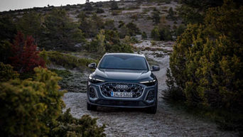 Front view of the 2025 Audi Q5 driving on a gravel road in a forested area.