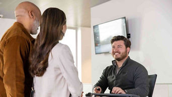 A couple speaking with an Audi Specialist at a desk. The Specialist is smiling at them.