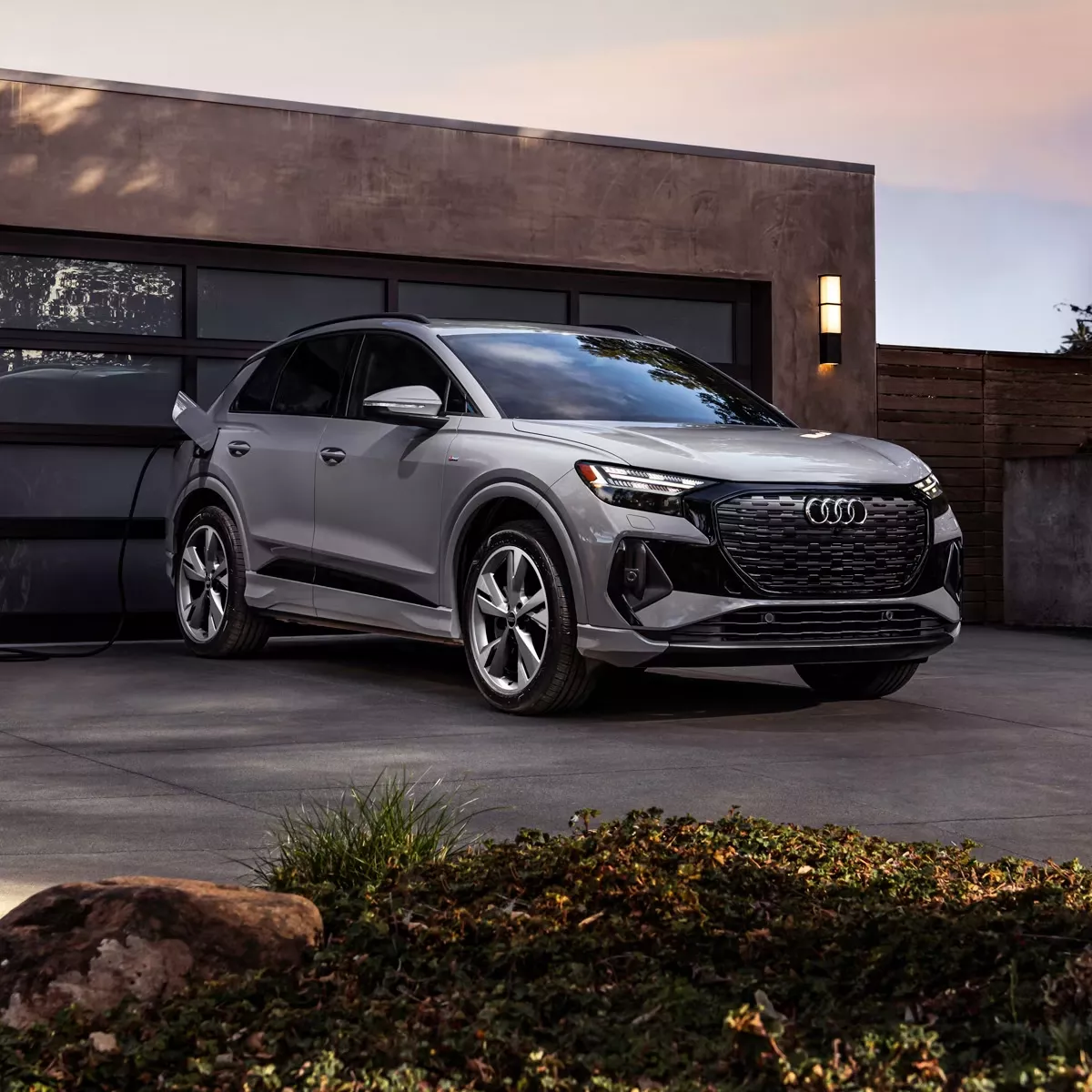 Three-quarter front-view of the Audi Q4 e-tron® charging in front of a person's home. 
