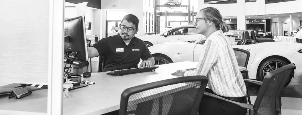 Audi sales specialist walking with a customer through the showroom. The sales specialist is handing the customer a key fob for an Audi vehicle. 