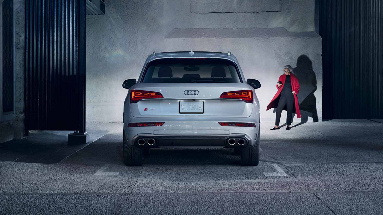 Rear view of an Audi vehicle with a woman standing to the right.