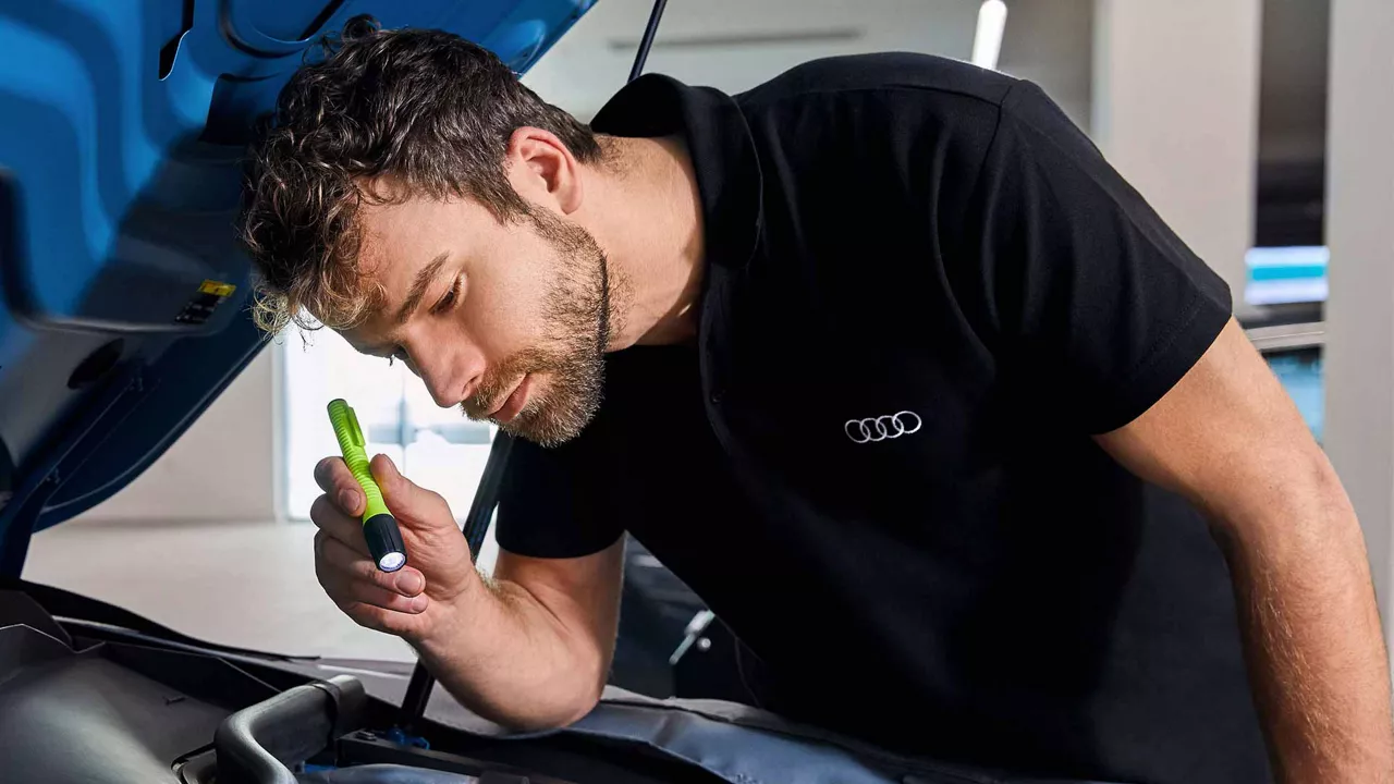 An Audi Technician inspecting the open hood of an Audi vehicle.