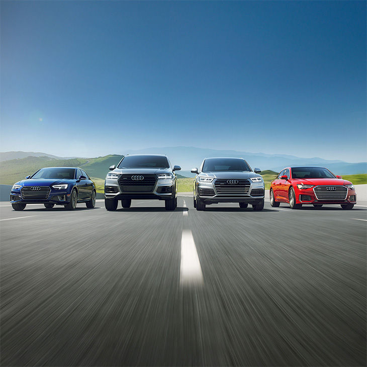 Front view of four Audi vehicles on an open road.