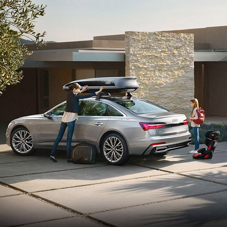 A woman closing the cargo box on top of an Audi vehicle with a girl standing behind the vehicle.