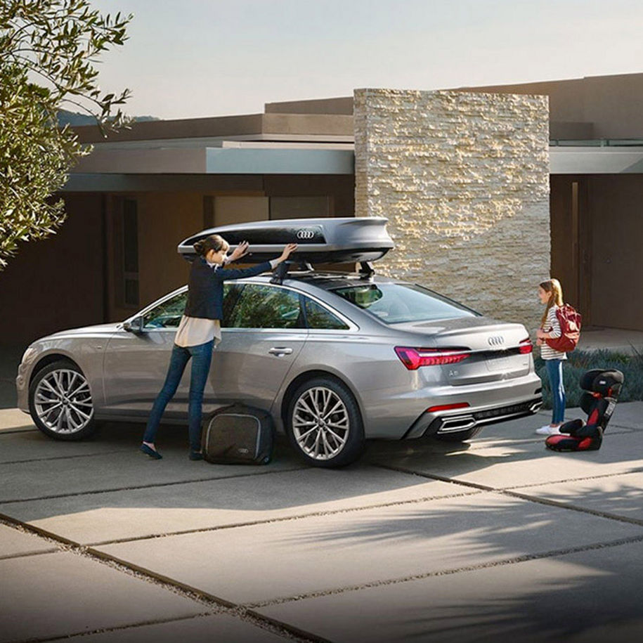 A woman closing the cargo box on top of an Audi vehicle with a girl standing behind the vehicle.