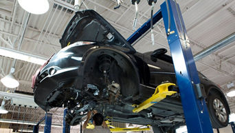 A mechanic works beneath a car on a lift in a garage.