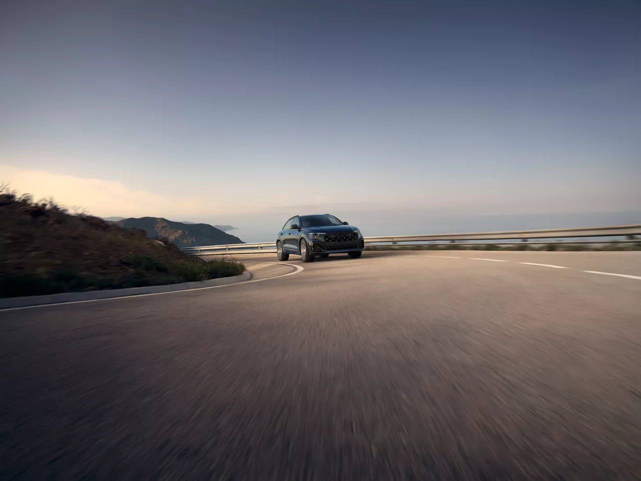 New 2025 Audi Q8 SUV cruising on a banked hilly road.