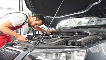 Service technician repairing vehicle with hood open.