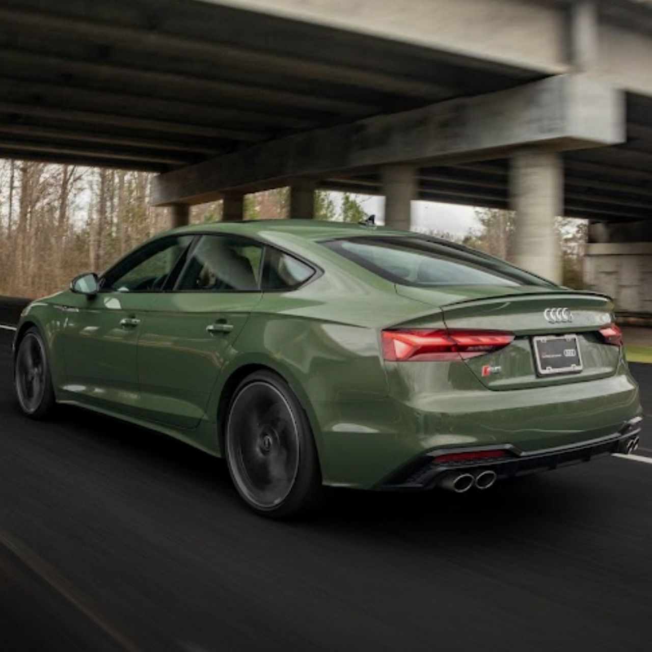 Rear view of a green Audi accelerating down the road. 