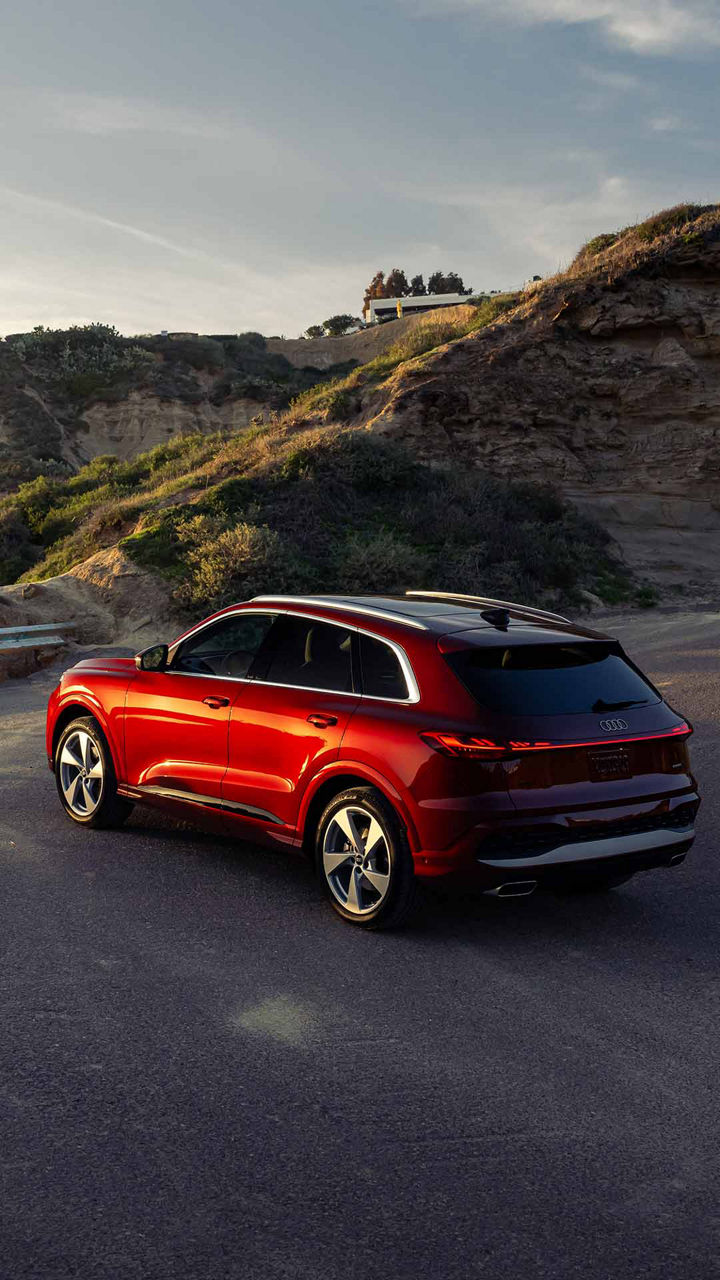 Red Audi driving up winding road at sunset