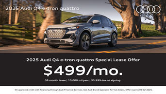 Three quarter view of an Audi q4 e-tron driving with trees in the the background.