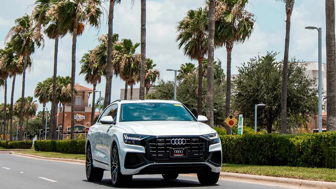 Front view of an Audi accelerating on a road near palm trees 