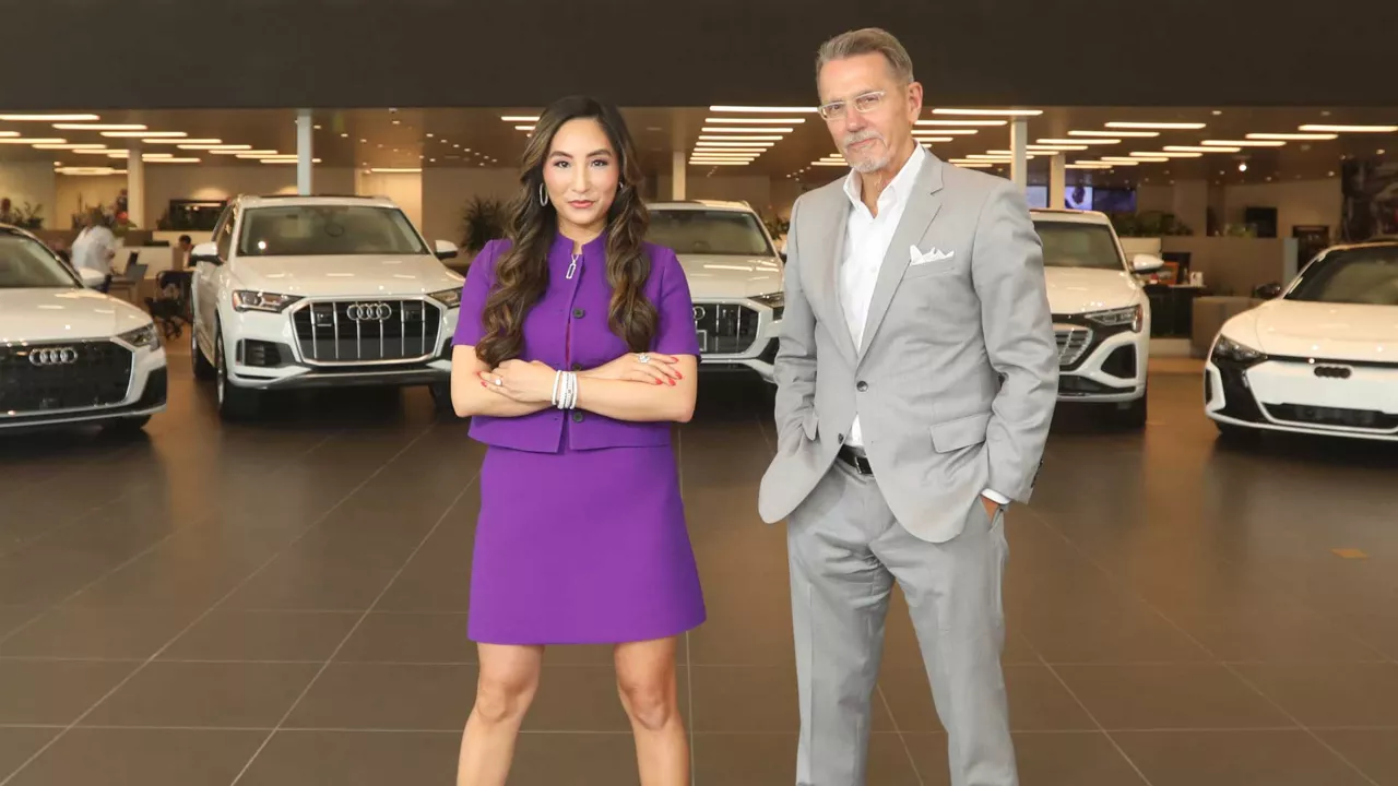 Two dealership employees in front of a fleet of Audi vehicles. 