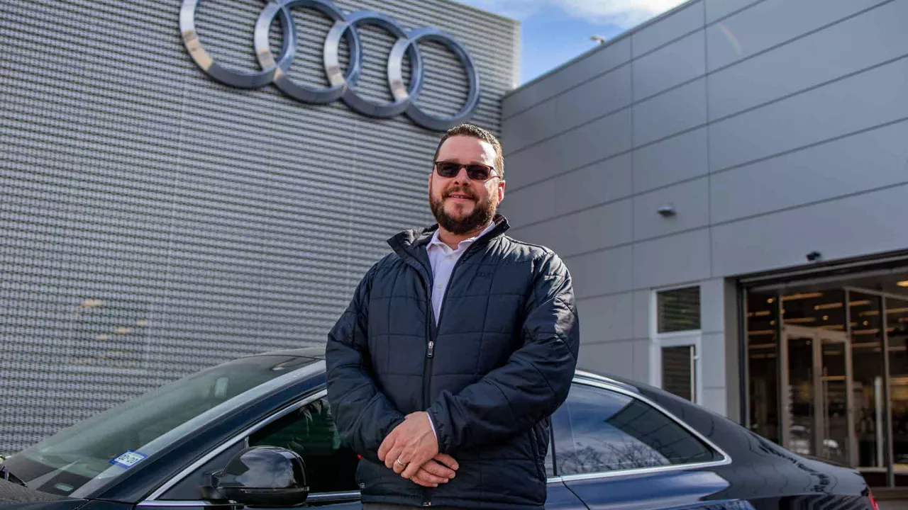 An Audi employee in front of an Audi vehicle and dealership building. 