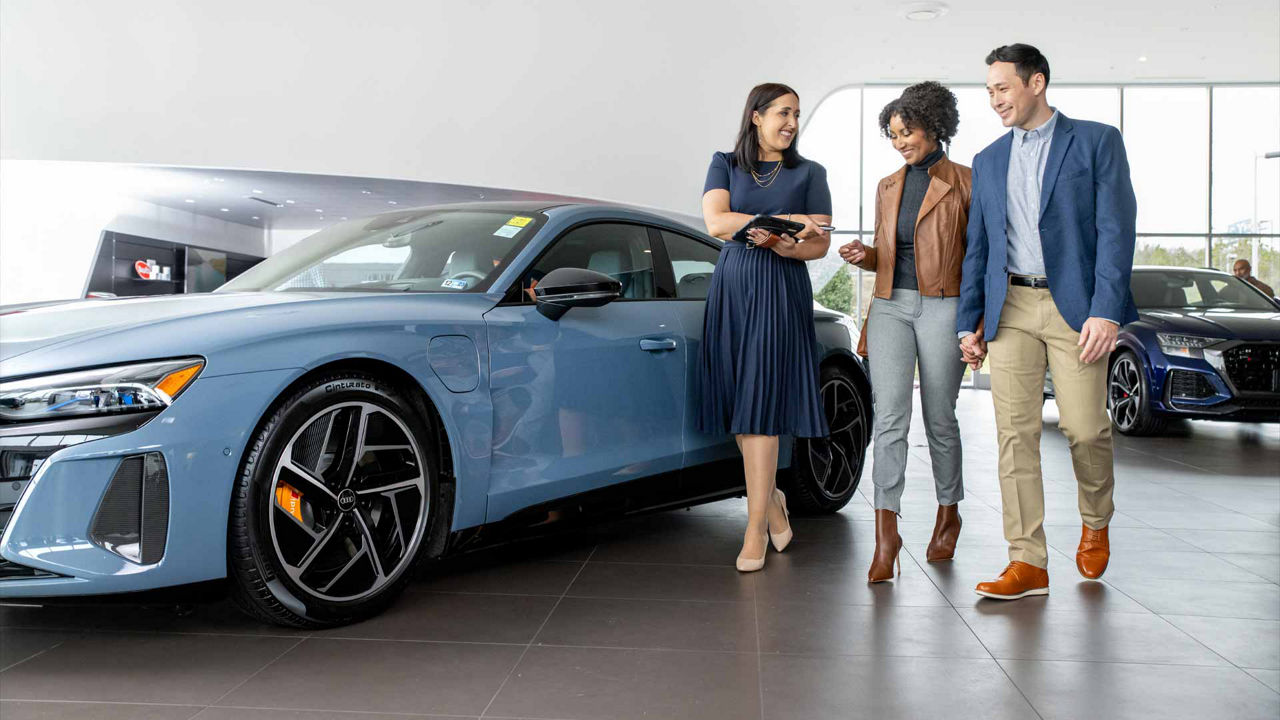 3 people standing beside an Audi in the showroom.