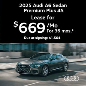 Audi A6 driving along road next to sidewalk and building