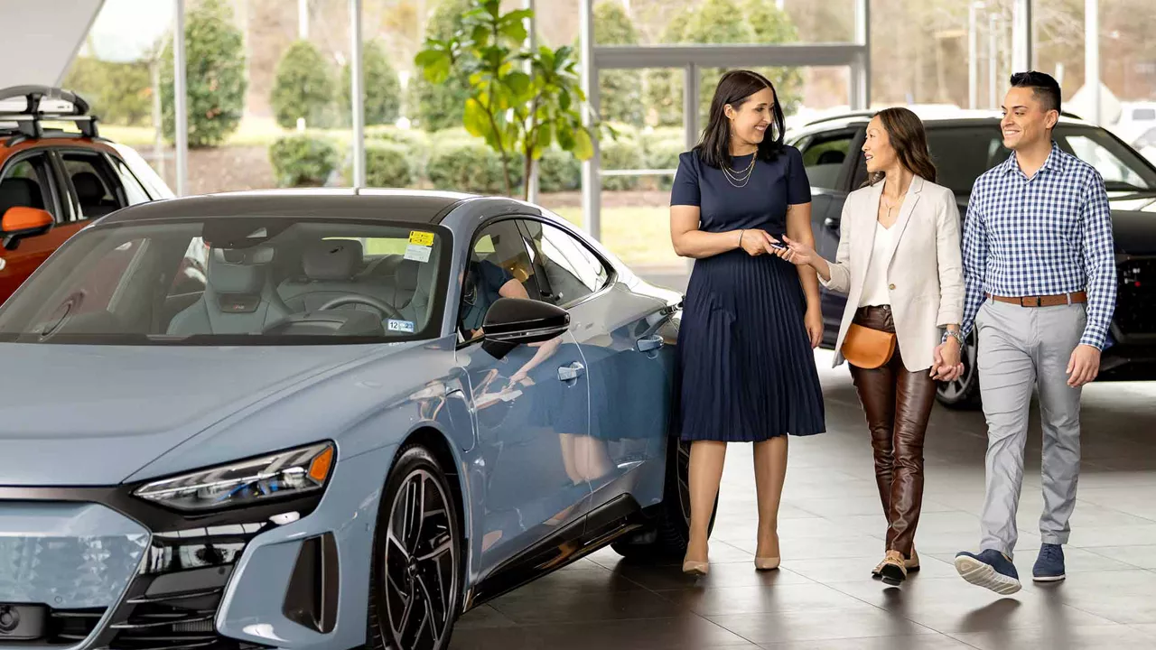 Audi sales specialist handing keys to woman and man in dealership showroom