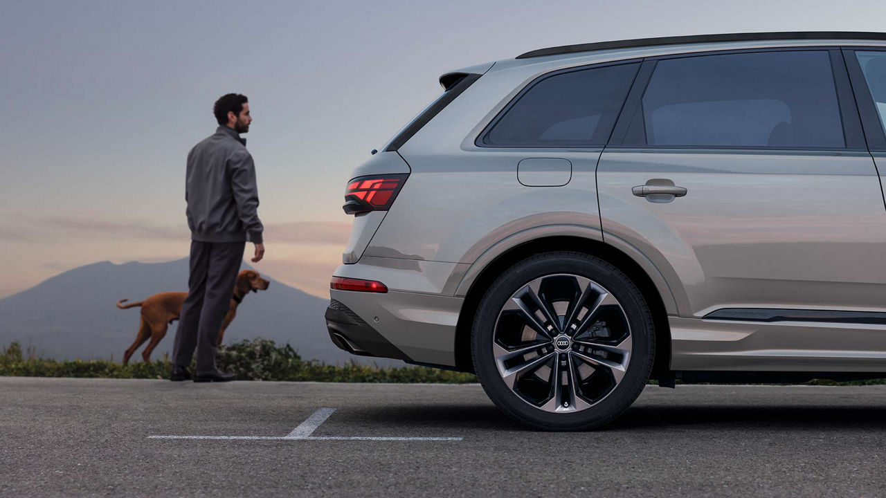 Close-up side view of a man standing next to the bumper of an Audi vehicle. 